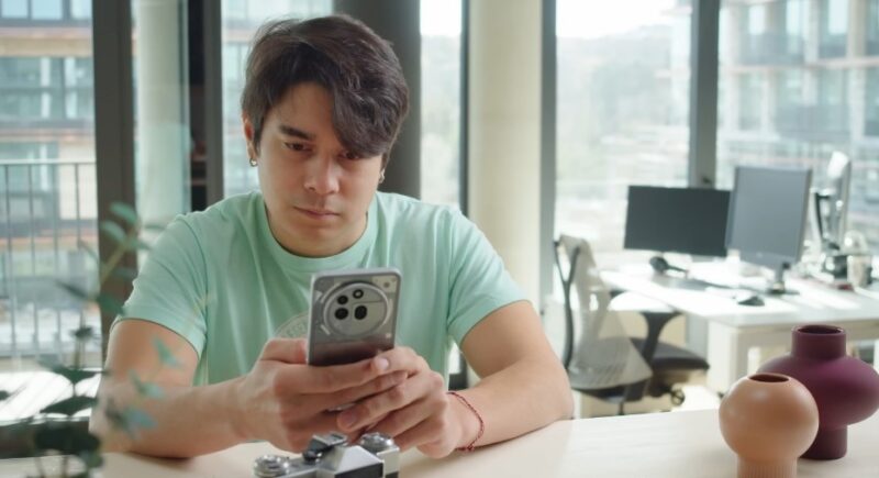 A man sits in an office, his attention directed to his smartphone
